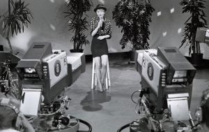 Schwarz weiß Aufnahme der Sängerin im Fernseh. Im Vordergrund stehen zwei Kameras, die sie filmen